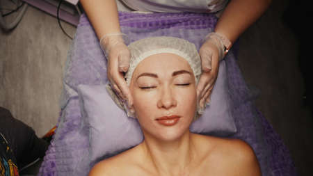 Woman receiving anti-ageing facial massage in spa salon relax. Wellness body skin care face beauty treatment. Black backgroundの写真素材