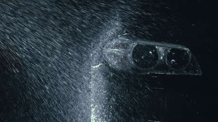 Car headlight wash. Washing modern vehicle body by high pressure jet wash hose water. Auto glass headlamp, angel eyes in drops.の写真素材