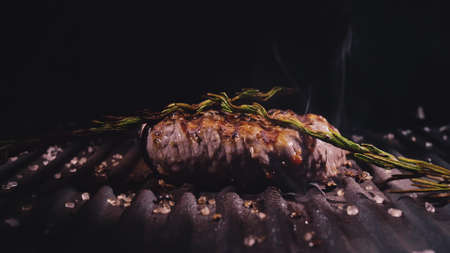Delicious juicy meat steak cooking on grill. Prime beef fry on electric roaster, rosemary, black pepper, salt. Slow motion.の写真素材