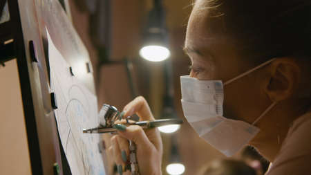 Woman artist learns to paint with airbrush with acrylic dye, paper and easel. Concept modern art, airbrushing, aerography, graffiti, aerosol sprayの写真素材