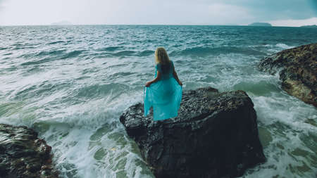 Woman meditates, relaxes on a rock reef hill in stormy morning rain cloudy sea. Concept feminine,...