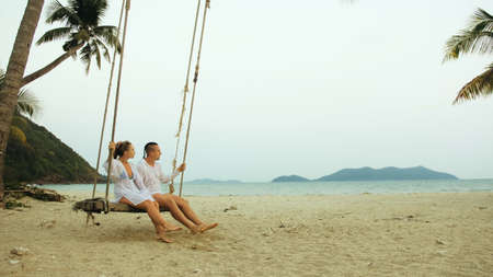 Loving couple on the swing on tropical beach. Woman and man in wの写真素材