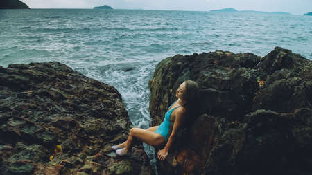 Woman meditates, relaxes on rock crack reef hill in stormy morning cloudy sea. Concept feminine, sexual vaginal health, womanly, freedom, freshnessの写真素材
