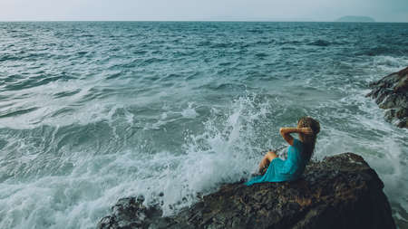 Woman meditates, relaxes on a rock reef hill in stormy morning rain cloudy sea. Concept feminine, relax, sexual health. Dark dramatic silhouette viewの写真素材