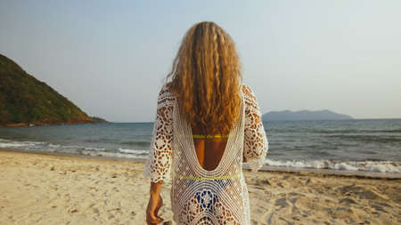 Woman in a white tunic on the beach, near the stormy sea. Blonde
