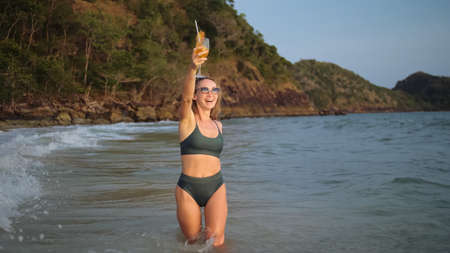 Woman stand knee-deep in sea on sunset. Girl on beach in green sの写真素材