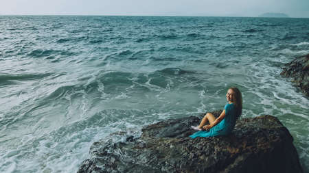 Woman meditates, relaxes on a rock reef hill in stormy morning rain cloudy sea. Concept feminine, relax, sexual health. Dark dramatic silhouette viewの写真素材