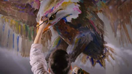 Artist designer draws an eagle on the wall. Craftsman decorator paints a picture with acrylic oil color looking at the sketch in the phone.の写真素材