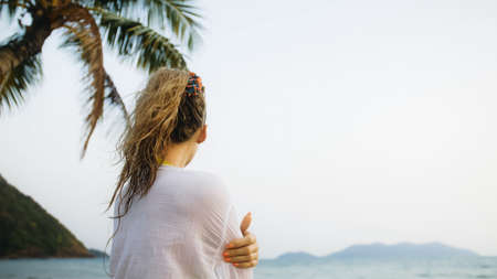 Woman in a white tunic shirt on beach, near sea, tilted palm treの写真素材