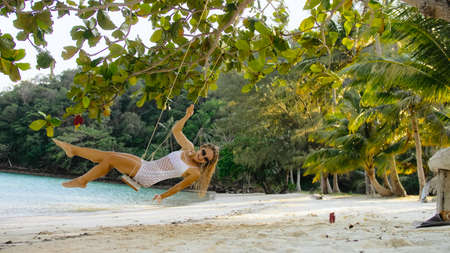 Radiant woman is swinging on a swing. Charming girl spends her vacation at the seaside. Concept...