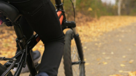 One caucasian children rides bike road in autumn park. Little girl riding black orange cycle in forest. Kid goes do bicycle sports. Biker motion ride with backpack and helmet. Mountain bike hard tail.の写真素材