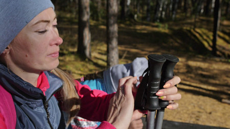 Woman do Nordic walking in nature. Girls and children use trekking sticks and nordic poles, backpacks. Family travels and goes in for sports. Autumn forest.の写真素材