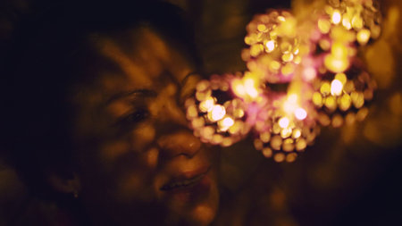 Magic hot light from lanterns falls on the woman eyes. The naked adult sexy caucasian girl lies at night on the bed and holds warm lamps in her hands.の写真素材