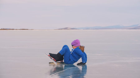 The child train on ice speed skating. The athlete stretches, warms up, rest. The kid girl skates in sportswear, sport glasses. Outdoor slow motion.の写真素材