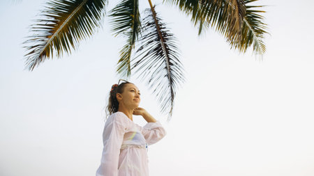 Woman in a white tunic shirt on beach, near sea, tilted palm treの写真素材