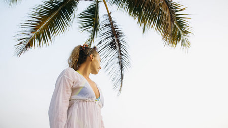 Woman in a white tunic shirt on beach, near sea, tilted palm treの写真素材