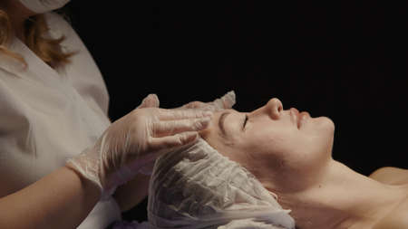 Woman receiving anti-ageing facial massage in spa salon relax. Wellness body skin care face beauty treatment. Black backgroundの写真素材