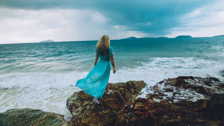 Woman meditates, relaxes on a rock reef hill in stormy morning rain cloudy sea. Concept feminine, relax, sexual health. Dark dramatic silhouette viewの写真素材