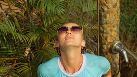 Woman taking a shower in garden near hotel. Girl in blue swimsui
