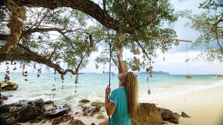 Pretty woman swinging on a swing on a tropical beach, on shores of the turquoise sea. Concept...