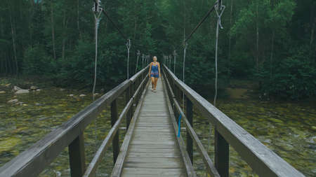 Woman Walking Along Suspension Bridge Alone in Picturesque Green Forest Setting.の写真素材