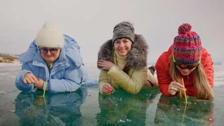 Siberia tradition cocktail Kiss of Baikal is entertainment for tourist on Lake Baikal.Three woman drink alcohol liquid without straw into makeshift glasses in hole frozen ice.Fun vacation trip travel.の写真素材
