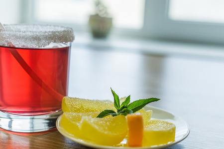 On a table there is a glass with a red fruit drink and fruit candy in a saucer.の写真素材