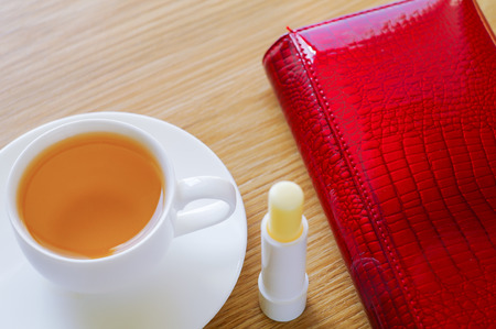 On a table there is a cup with green tea, lipstick and lies a red purse.の写真素材