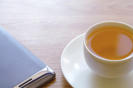 On a table there is a cup with green tea on a saucer and the smart phone lies.の写真素材