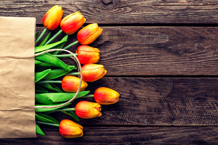 Bouquet of tulips in a paper shopping bag on a wooden background, concept of discounts and sales on the Women's Day or Mother's Day or Easterの写真素材