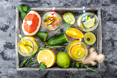 Variety of fruit infused detox water in glass jars and ingredients for preparing top view on dark stone backgroundの写真素材