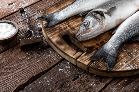 fresh raw sea bass fish on wooden cutting board cooking concept on a dark wooden background top viewの写真素材