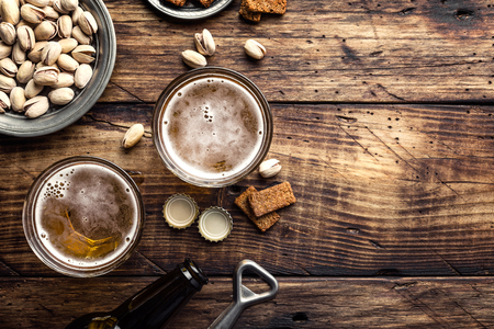 Two glasses of fresh beer and salty snacks on a brown wooden table, top view and space for textの写真素材