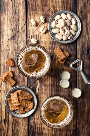 Two glasses of fresh beer and salty snacks on a brown wooden table, top viewの写真素材
