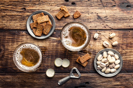 Two glasses of fresh beer and salty snacks on a brown wooden table, top view の写真素材