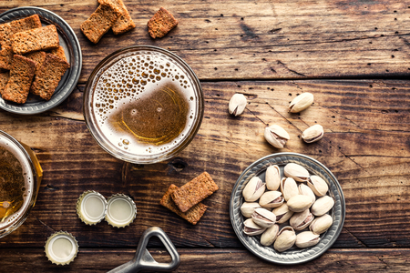Two glasses of fresh beer and salty snacks on a brown wooden table, top view and space for textの写真素材