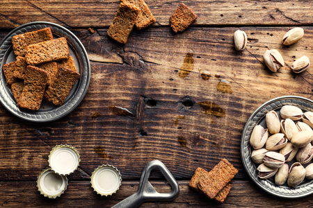 food background with salty snacks and beer bottle caps on old brown wooden table top with space for your text, beer party conceptの写真素材