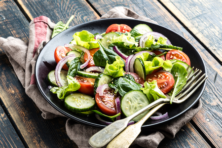 Healthy vegetable salad of fresh tomato, cucumber, spinach, onion and lettuce on plate. Diet menuの写真素材