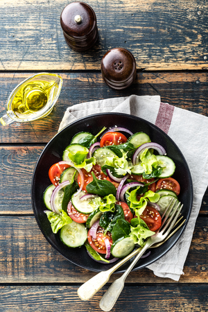 Healthy vegetable salad of fresh tomato, cucumber, spinach, onion and lettuce on plate. Diet menu. Top view.の写真素材