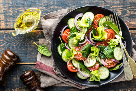 Healthy vegetable salad of fresh tomato, cucumber, spinach, onion and lettuce on plate. Diet menu. Top view.の写真素材