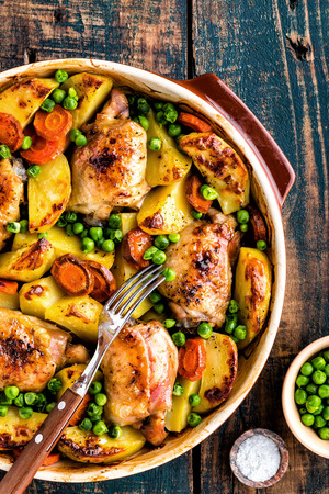 Chicken thighs baked with potato, carrot and green peasの写真素材