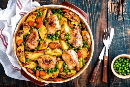 Chicken thighs baked with potato, carrot and green peasの写真素材
