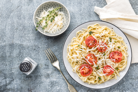 cooked noodles on a table in a plate with tomatoes, parmesan cheese and spicesの写真素材