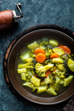 plate of fresh hot vegetable soup with broccoli, potato, green peas, onion and carrot. healthy vegan diet food, top viewの写真素材