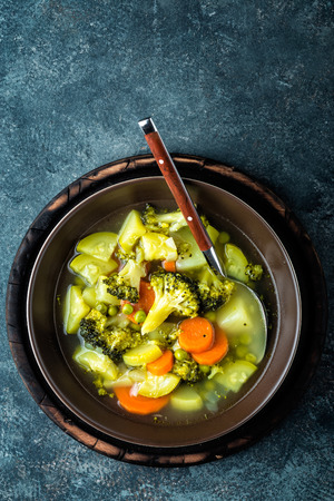 plate of fresh hot vegetable soup with broccoli, potato, green peas, onion and carrot. healthy vegan diet food, top viewの写真素材