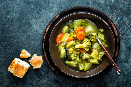 plate of fresh hot vegetable soup with broccoli, potato, green peas, onion and carrot. healthy vegan diet food, top viewの写真素材