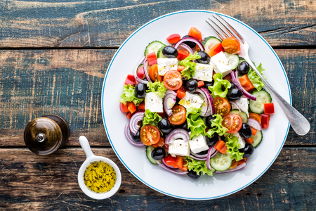 Greek salad of fresh cucumber, tomato, sweet pepper, lettuce, red onion, feta cheese and olives with olive oil. Healthy food, top viewの写真素材
