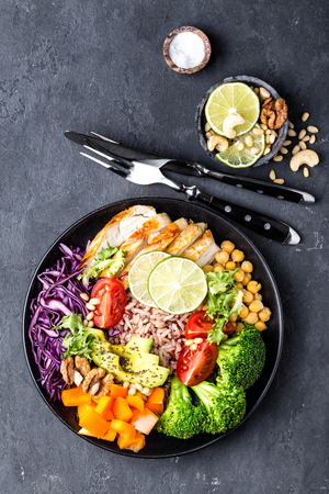 Buddha bowl dish with chicken fillet, brown rice, avocado, pepper, tomato, broccoli, red cabbage, chickpea, fresh lettuce salad, pine nuts and walnuts. Healthy balanced eating. Top viewの写真素材