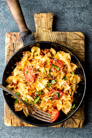 pasta farfalle with roasted meat and tomatoes in a frying panの写真素材