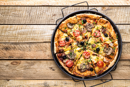 pizza with cheese, tomatoes, mushrooms, ham, sausage and olives on a wooden table, top viewの写真素材